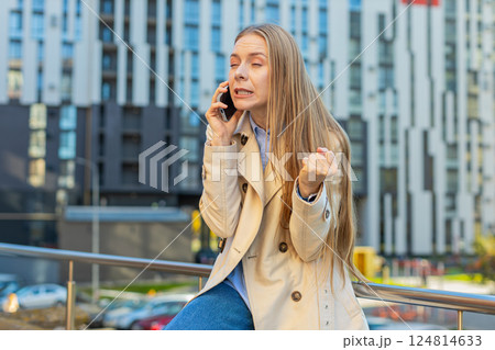Caucasian mature businesswoman girl in coat arguing talking on smartphone on downtown city street Caucasian mature businesswoman girl in coat arguing talking on smartphone on downtown city street 124814633