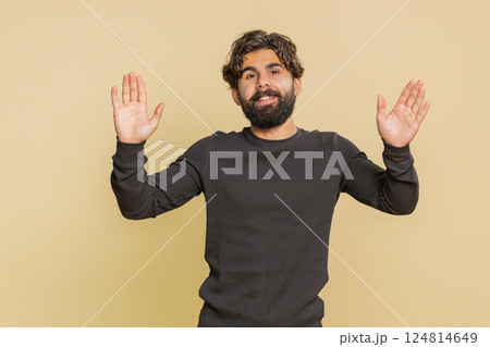 Handsome young Indian man with long sleeves waving hello with his palm against beige background 124814649