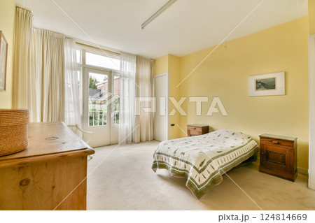 A spacious bedroom featuring warm yellow walls, large windows, and simple furnishings. Perfectly designed for comfort and relaxation in a serene environment. A spacious bedroom featuring warm yellow walls, large windows, and simple furnishings. Perfectly designed for comfort and relaxation in a serene environment. 124814669