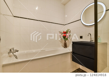 A sleek bathroom featuring a spacious bathtub, stylish sink, and elegant floral arrangement, emphasizing contemporary design and functionality. A sleek bathroom featuring a spacious bathtub, stylish sink, and elegant floral arrangement, emphasizing contemporary design and functionality. 124814918