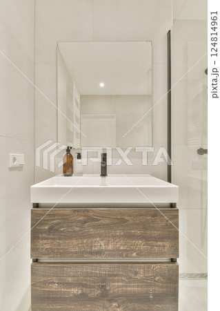 A sleek, modern bathroom featuring a wooden vanity, large mirror, and minimal decor, creating a serene and stylish atmosphere. 124814961