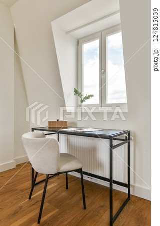A sleek home office featuring a minimalistic desk, cozy chair, and window enhancing the workspace with ample natural light. 124815039