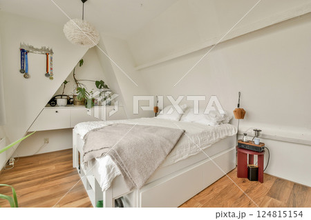 A serene minimalist bedroom featuring a comfortable bed with light bedding, wooden flooring, and small plants for a touch of nature. Simple yet elegant decor elements enhance tranquility. 124815154
