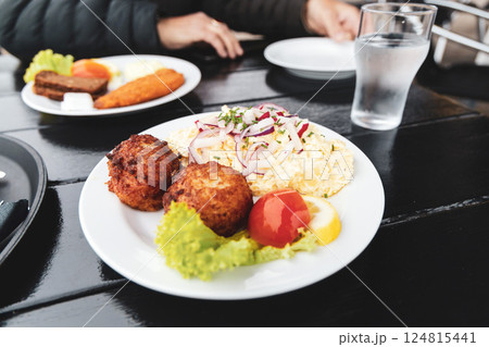 Seafood restaurant on the seashore. White plate with fish patties, fish fillets and potato salad. 124815441