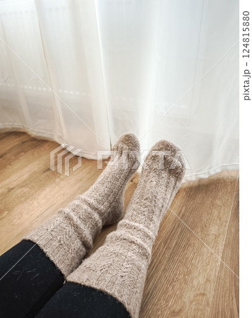Woman resting near window and next to the heating in prague, wearing soft knitted socks, enjoying peaceful indoor atmosphere with warm light Galentines day Woman resting near window and next to the heating in prague, wearing soft knitted socks, enjoying peaceful indoor atmosphere with warm light Galentines day 124815880