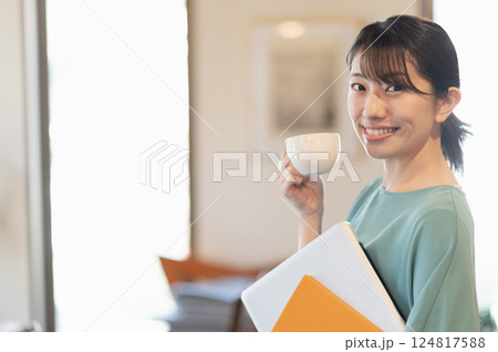 ノートパソコンを持ちながら立ってコーヒーを飲む女性 124817588