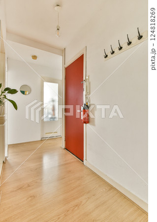 A bright and modern entryway featuring a striking red door, wooden flooring, and minimalist decor that welcomes visitors with an airy feel. 124818269