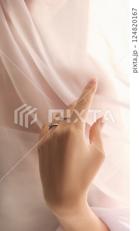 Cropped image of gentle female hands with two elegant, minimalistic silver rings against a softly draped, light-colored fabric. 124820167