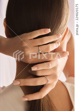 Back view, close-up image of woman demonstrating two minimalistic silver rings against light, soft background. 124820175