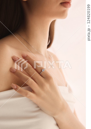 Cropped side view portrait of woman with engagement ring and silver necklace, radiating soft beauty and romantic charm 124820199