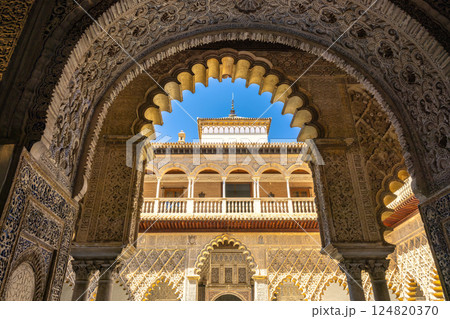 The Alcazar of Seville, historic royal palace in Seville town, Andalusia, Spain. Ornate archway framing a sunlit palace courtyard. Intricate stonework and a clear blue sky. The Alcazar of Seville, historic royal palace in Seville town, Andalusia, Spain. Ornate archway framing a sunlit palace courtyard. Intricate stonework and a clear blue sky. 124820370