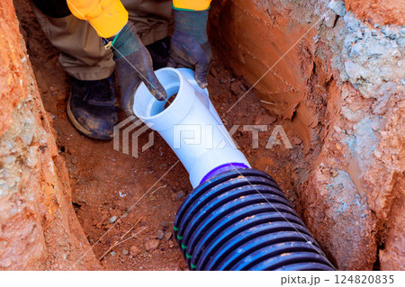 Construction worker connect drainage pipes in trench to ensure drainage water flow at construction site 124820835