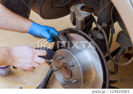 Technician works on vehicle's brake system, adjusting components with care precision in well lit workshop. Technician works on vehicle's brake system, adjusting components with care precision in well lit workshop. 124820861