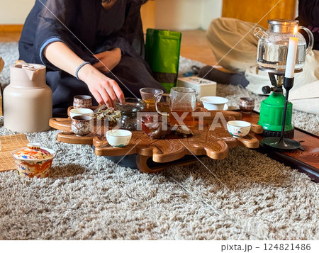 A woman pours yellow tea during a traditional gongfu tea ceremony on a carved wooden tray. Ritual, attention and mindfulness through tea preparation A woman pours yellow tea during a traditional gongfu tea ceremony on a carved wooden tray. Ritual, attention and mindfulness through tea preparation 124821486