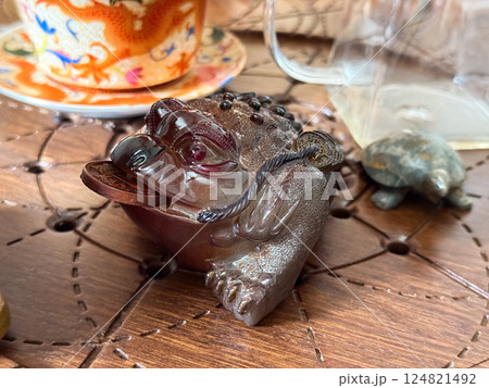 Fortune frog with coin on tea table during traditional tea ritual. Prosperity, symbolism and harmony within the tea ceremony atmosphere Fortune frog with coin on tea table during traditional tea ritual. Prosperity, symbolism and harmony within the tea ceremony atmosphere 124821492