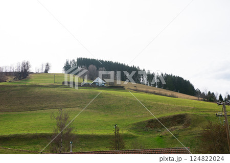 Beneath a vast, cloudy sky, rolling green hills cradle a solitary house, creating a picture-perfect scene in a serene countryside landscape Beneath a vast, cloudy sky, rolling green hills cradle a solitary house, creating a picture-perfect scene in a serene countryside landscape 124822024