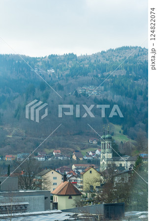 Nestled among misty hills, picturesque village showcases charming architecture and a tranquil church steeple beneath a gray winter sky Nestled among misty hills, picturesque village showcases charming architecture and a tranquil church steeple beneath a gray winter sky 124822074