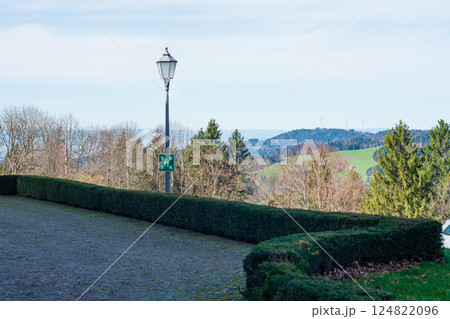 Strolling along a serene pathway lined with hedges, enjoying a peaceful afternoon in the countryside with distant mountains and gentle hills in view Strolling along a serene pathway lined with hedges, enjoying a peaceful afternoon in the countryside with distant mountains and gentle hills in view 124822096