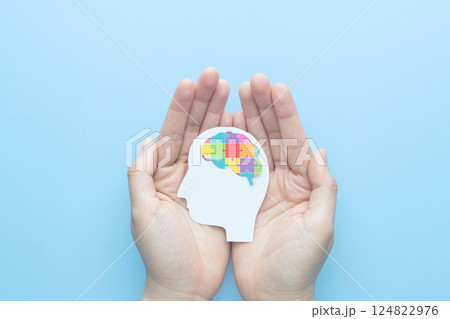 World autism awareness day concept. Hands holding human head shape with colorful jigsaw puzzle brain on blue background. Creative idea for Autism Spectrum Disorder (ASD). 124822976