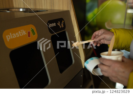 Person throwing ice cream spoon into recycling bin, sorting waste, environmental protection 124823029