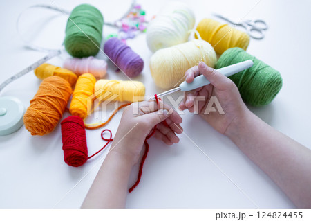 Child crocheting with colorful yarn balls and crochet hook Child crocheting with colorful yarn balls and crochet hook 124824455