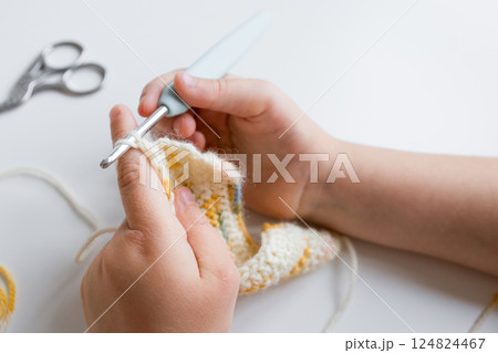 Close up of young caucasian child crocheting with yellow and white yarn 124824467