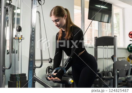 Young woman training on cable machine in gym. Young woman training on cable machine in gym. 124825487