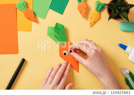 Making a simple origami carrot Easter craft. Glue on the funny eyes. Around the paper creativity tools. Making a simple origami carrot Easter craft. Glue on the funny eyes. Around the paper creativity tools. 124825661