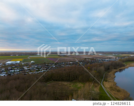A scenic aerial view of a peaceful rural landscape at dawn, featuring farmlands, colorful flower fields, a quiet village, forested areas, and a calm lake under a cloudy sky. A scenic aerial view of a peaceful rural landscape at dawn, featuring farmlands, colorful flower fields, a quiet village, forested areas, and a calm lake under a cloudy sky. 124826611