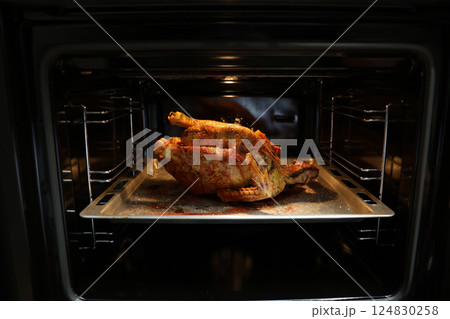 Festive christmas roast whole duck on aluminized steel baking sheet inside open oven at home kitchen. Ready golden turkey or goose on tray. Classic American Thanksgiving food preparation. 124830258