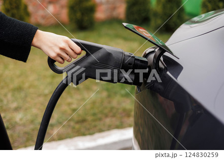 Unrecognisable woman inserting EV charger plug from public or home charging station for modern electric or hybrid car at special place for e-car. Concept eco-friendly sustainability energy car Unrecognisable woman inserting EV charger plug from public or home charging station for modern electric or hybrid car at special place for e-car. Concept eco-friendly sustainability energy car 124830259