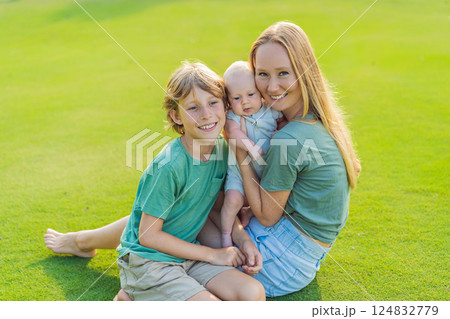 Mother, older son, and newborn baby on a meadow in the park. Family spending quality time together in nature. Parenthood, love, and family bond concept Mother, older son, and newborn baby on a meadow in the park. Family spending quality time together in nature. Parenthood, love, and family bond concept 124832779