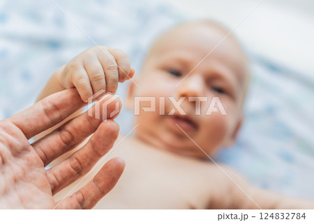 Newborn baby lying on a soft blanket, gently holding fathers finger. Love, bonding, and parenthood concept Newborn baby lying on a soft blanket, gently holding fathers finger. Love, bonding, and parenthood concept 124832784