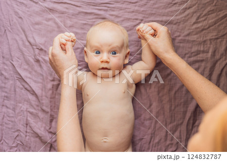 Newborn baby lying on a soft blanket while mother gently exercises the babys tiny limbs. Early development, bonding, and baby care concept 124832787