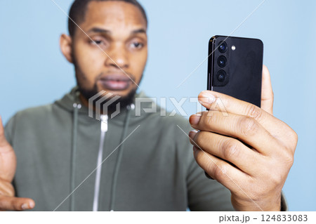 Confident upbeat young man talking to his mates on online call, using his smartphone to keep in touch and contact his group of friends. Social person in a relaxed conversation. Confident upbeat young man talking to his mates on online call, using his smartphone to keep in touch and contact his group of friends. Social person in a relaxed conversation. 124833083