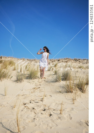 Carefree woman in white dress walking barefoot across sunny sand dune landscape Carefree woman in white dress walking barefoot across sunny sand dune landscape 124833561