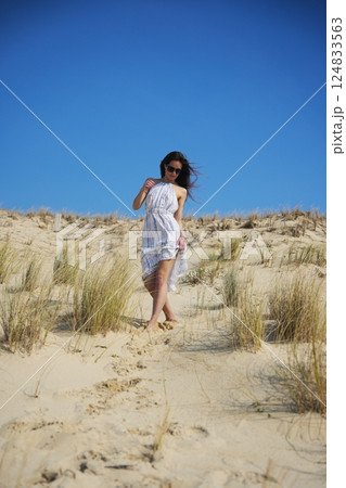 Woman walking barefoot on sandy dune under cloudless summer sky Woman walking barefoot on sandy dune under cloudless summer sky 124833563