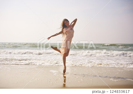 Ballet dancer performs elegant pose on beach. Flowing dress with ocean backdrop 124833617
