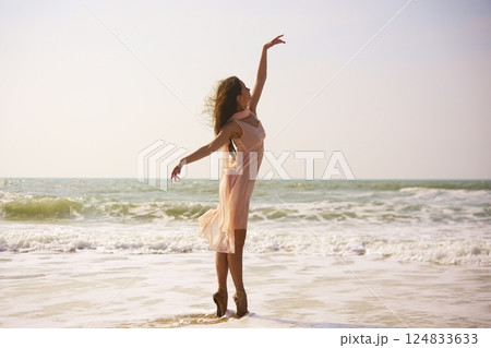 Ballet dancer on pointe by the ocean in a soft pink dress under sunset light Ballet dancer on pointe by the ocean in a soft pink dress under sunset light 124833633