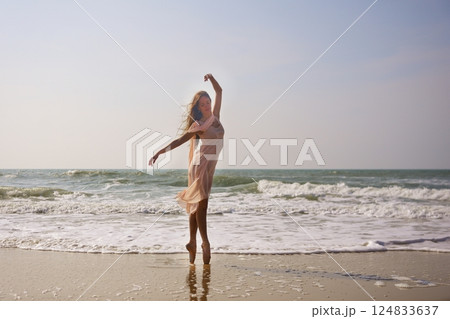 Graceful ballerina dancing en pointe on beach with flowing dress and ocean waves 124833637