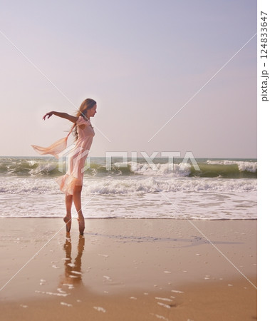 Graceful ballerina on pointe by the sea wearing a flowing pink dress at sunset Graceful ballerina on pointe by the sea wearing a flowing pink dress at sunset 124833647