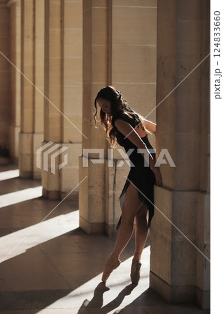 Ballet dancer en pointe leaning gently on column in sunlit stone corridor 124833660