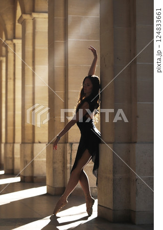 Ballet dancer en pointe by stone column in warm classical sunlit corridor 124833661