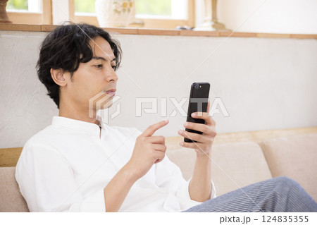 ソファーに座ってスマホを操作する若い男性 124835355