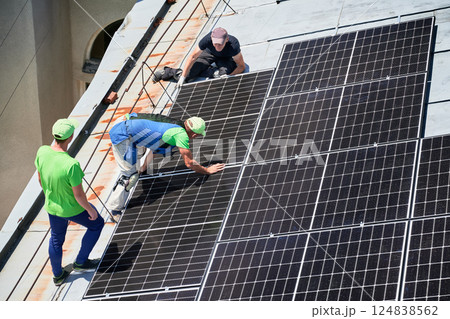 Workers building solar panel system on metal rooftop of house. Three men installers installing photovoltaic solar module outdoors. Alternative, green and renewable energy generation concept. 124838562
