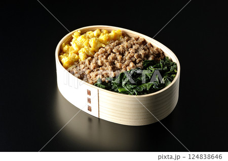 卵、肉、ほうれん草の三色弁当を黒背景で撮影 124838646