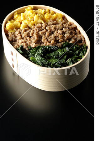 卵、肉、ほうれん草の三色弁当を黒背景で撮影 124838659