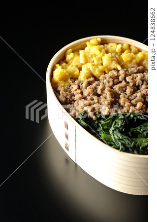 卵、肉、ほうれん草の三色弁当を黒背景で撮影 124838662