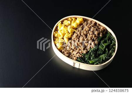 卵、肉、ほうれん草の三色弁当を黒背景で撮影 124838675