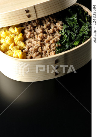 卵、肉、ほうれん草の三色弁当を黒背景で撮影 124838694